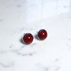 May include: A pair of silver stud earrings with red glitter round cabochons.