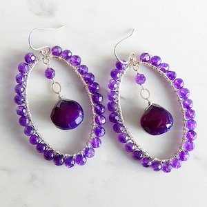 May include: A pair of silver hoop earrings with a dangling amethyst gemstone. The hoops are made of wire wrapped with amethyst beads.