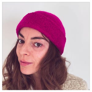 May include: A woman wearing a bright pink fleece beanie hat. The hat is folded over at the top and has a textured surface.