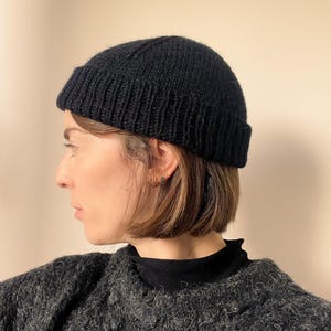 Op de afbeelding: Een zwarte gebreide beanie met een simpel ontwerp. De muts is gemaakt van een zacht, warm materiaal en is perfect voor koud weer.