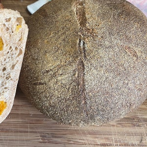 May include: A close-up of a loaf of sourdough bread with a golden brown crust and a soft, white interior. The bread is sliced open, revealing a bright orange filling of apricot or peach pieces. The bread is sitting on a wooden cutting board.