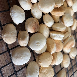 May include: A close-up of a wire rack filled with small, round, light brown crackers. The crackers are arranged in a random pattern and some are stacked on top of each other.