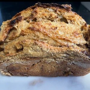 May include: A close-up of a loaf of freshly baked bread with a crusty, golden brown exterior. The bread has a slightly irregular shape and a soft, airy texture.