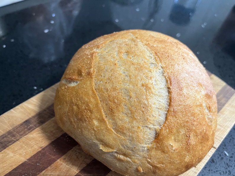 以下が含まれることがあります： こんがりと焼けた皮のついた、焼き立てのパン。パンは少し不揃いな形をしていて、中央に深くはっきりとした切れ込みが入っています。