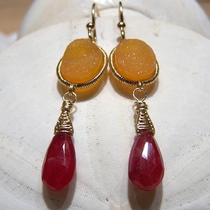 Può includere: Orecchini avvolti in filo d'oro con una pietra rossa a forma di lacrima e una pietra rotonda arancione.