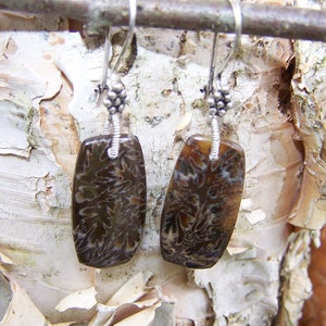 Op de afbeelding: Een paar zilveren oorbellen met hangers van versteend steen. De stenen zijn rechthoekig en hebben een bruin en wit marmerpatroon.