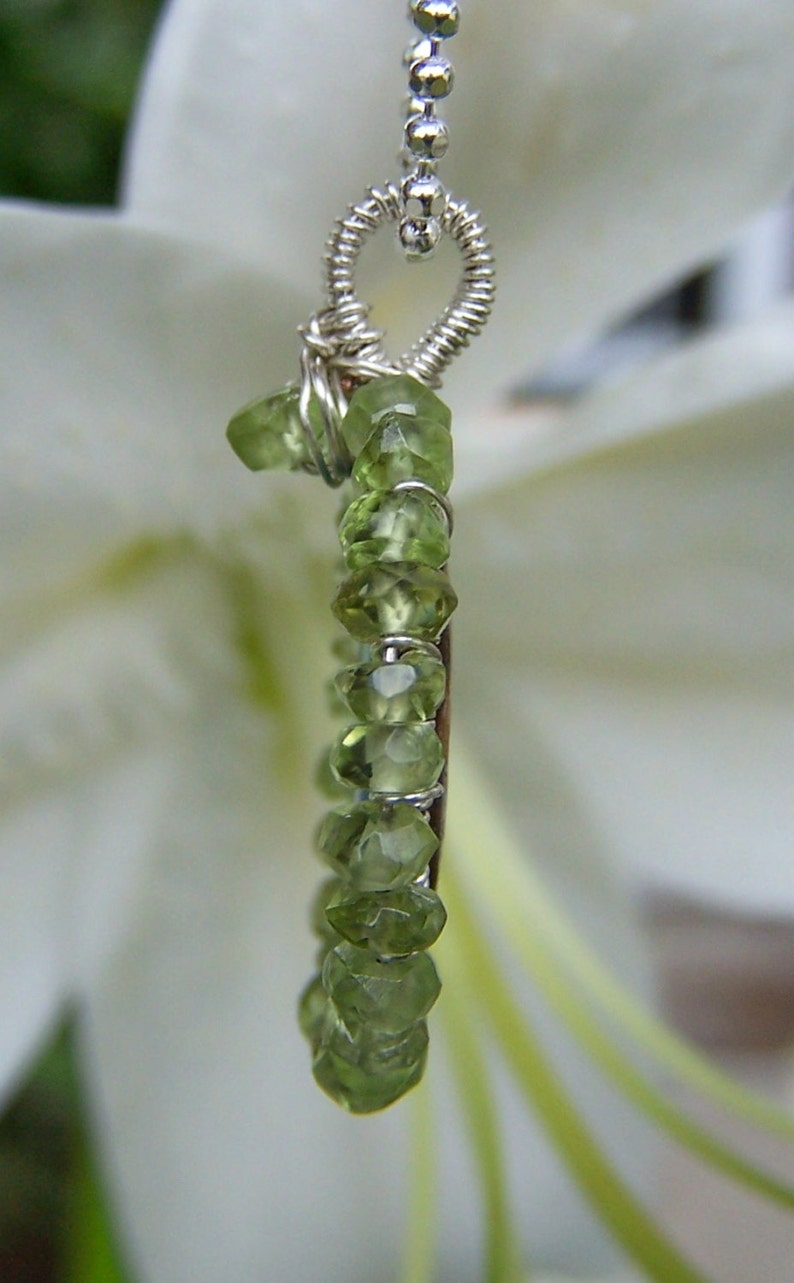 Pu&ograve; includere: Una collana con catena d'argento con un ciondolo a forma di cuore e una fila di peridoti verdi.