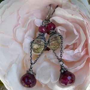 May include: A pair of silver earrings with a dangling design. Each earring features a yellow and a red gemstone, wrapped in silver wire.