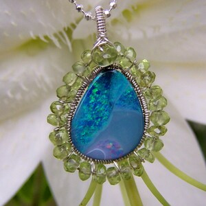 Pu&ograve; includere: Una collana con catena d'argento con un ciondolo a forma di lacrima in opale circondato da perline di peridoto verde.