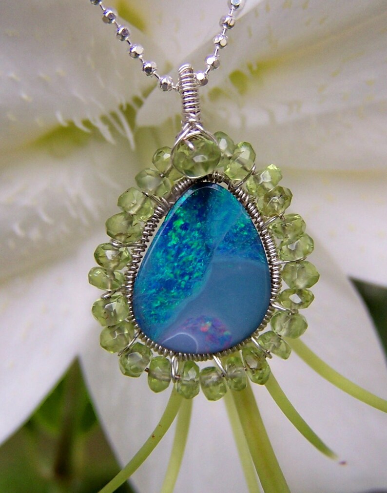 Pu&ograve; includere: Una collana con catena d'argento con un ciondolo a forma di lacrima in opale circondato da perline di peridoto verde.