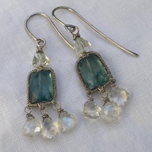 May include: A pair of silver dangle earrings with a green gemstone and clear crystal accents.