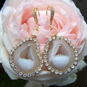 May include: A pair of gold earrings with a white agate stone set in a gold bezel and surrounded by clear rhinestones.