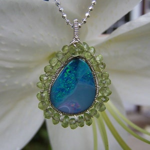 Pu&ograve; includere: Una collana con catena d'argento con un ciondolo a forma di lacrima che presenta una pietra preziosa di opale blu e verde circondata da perline di peridoto verde.