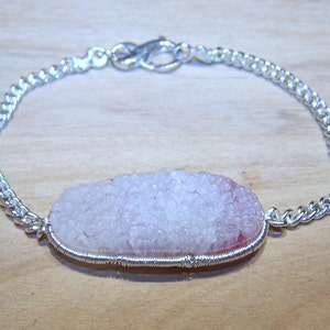 Pode incluir: Um bracelete de corrente de prata com um pingente de ágata rosa e branca. O pingente é envolto em fio de prata.
