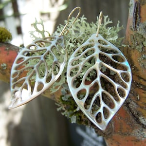 May include: A pair of silver leaf-shaped earrings with a delicate, intricate design. The earrings are made of a translucent material with a pearlescent finish.