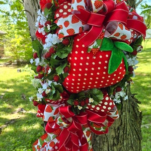 以下が含まれることがあります： 赤と白のイチゴをテーマにしたリースで、中央には大きく赤い白ドットのイチゴがあります。リースは赤と白のリボンと緑の葉で飾られています。