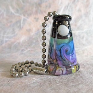 May include: A conical glass ceiling fan pull chain ornament featuring a swirling pattern of blue, purple, and green colors. The top section is black with a white circular accent, and the piece is attached to a silver-toned metal ball chain.