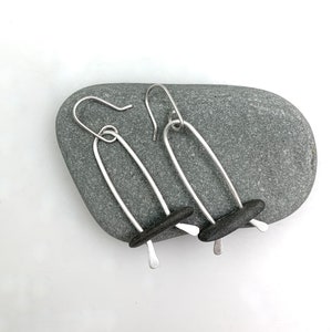 May include: A pair of silver earrings with black stone accents. The earrings are shaped like a long oval with a small stone at the bottom.