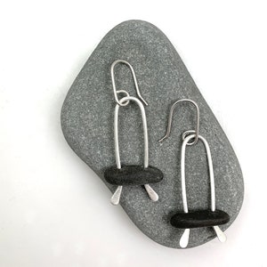 May include: A pair of silver earrings with black stone accents. The earrings are made of thin silver wire and have a simple, modern design.