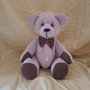 May include: A handmade teddy bear with a striped pattern in shades of brown and white. The bear has a brown bow tie and matching accents on its paws and ears. It is sitting on a light brown surface.