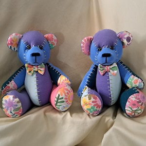 May include: Two handmade teddy bears with blue, purple, and white color blocks. The bears have floral patterned ears, paws, and belly accents. Each bear wears a bow tie and has stitched details.