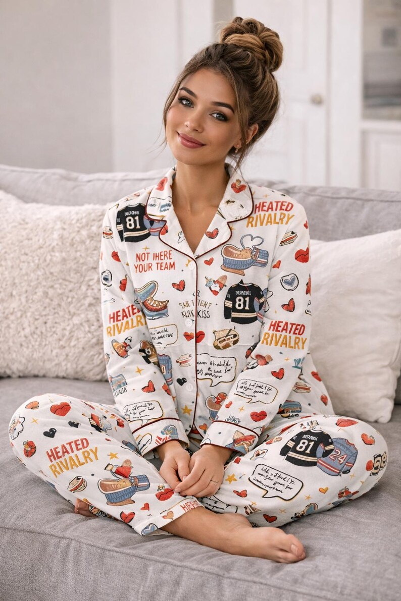 May include: White pajama set with a repeating pattern of hockey jerseys, hearts, and text. The long-sleeved top and pants feature red trim and the words "HEATED RIVALRY" and "NOT HERE YOUR TEAM".