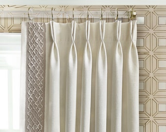 May include: Cream-colored pleated curtains with a decorative border featuring a woven pattern. The curtains hang from a gold-colored rod with rings. The background shows a geometric patterned wallpaper.