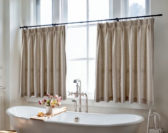 Puede incluir: Una bañera blanca con una bandeja de madera y flores en un jarrón blanco. La bañera está en un baño con dos ventanas con cortinas de lino beige.
