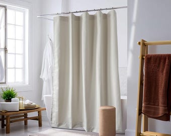 Può includere: Una tenda da doccia bianca è appesa in un bagno con un portasciugamani in legno e un asciugamano marrone. La tenda da doccia è realizzata in un tessuto morbido e liscio.
