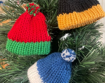 May include: Three knitted Christmas ornaments shaped like hats. The hats are red and green, black and gold, and blue and white.