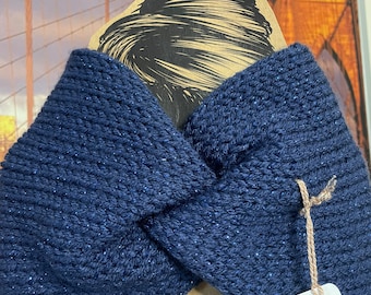 May include: A navy blue knitted headband with a twisted knot design. The headband is displayed on a cardboard cutout with a drawing of a woman's hair. A tag with the brand name is attached to the headband.