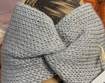 May include: A gray knitted headband with a twist design. The headband has a subtle sparkle and is made of a soft, textured yarn. The accessory is designed to keep hair out of the face.