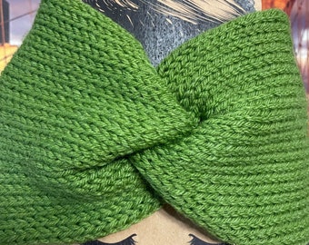 May include: A green knitted headband with a twisted knot design. The headband is made of a thick, textured yarn. The brand name "Fizz Pop Co." is printed at the bottom of the display.