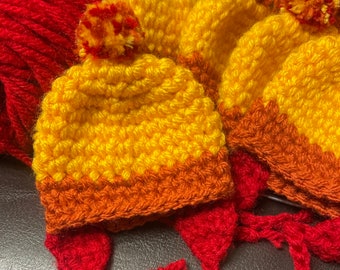 May include: A set of three crocheted hats in yellow, orange, and red. The hats have pom-poms on top and are made with a textured stitch.