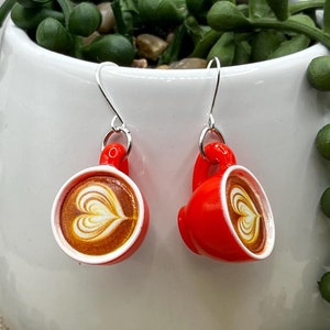 May include: A pair of red coffee cup earrings with a white heart design. The earrings are hanging from silver hooks.