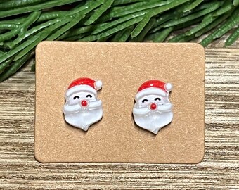 May include: A pair of Santa Claus stud earrings on a brown card. The earrings are white with red hats and white beards.