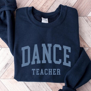 May include: A navy blue sweatshirt with the text "DANCE TEACHER" in a gray, collegiate-style font.