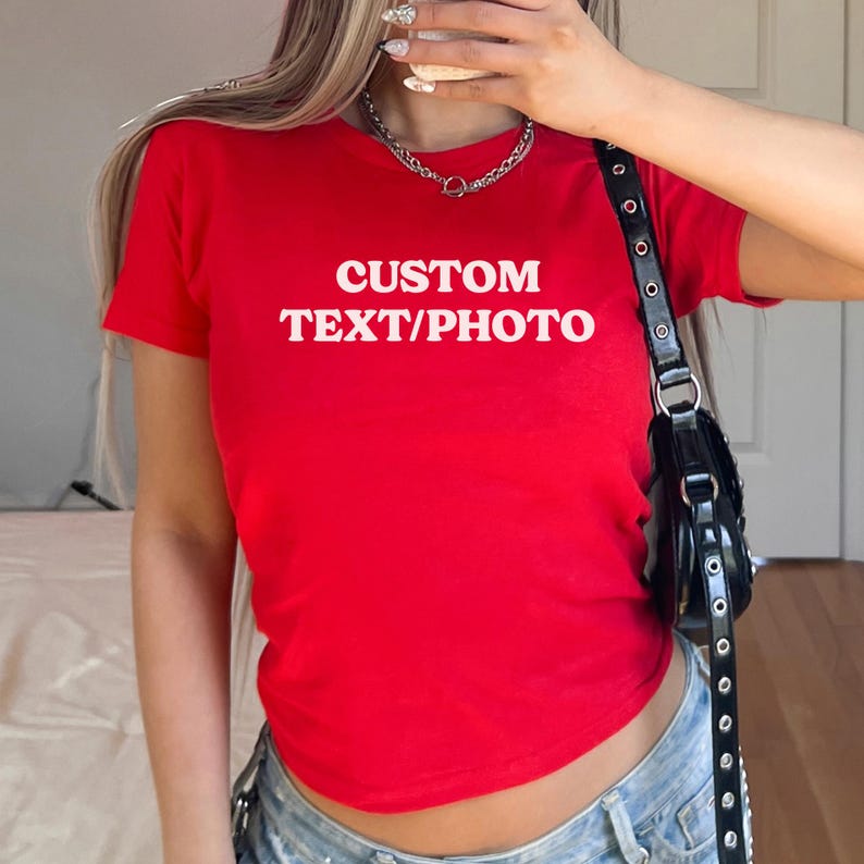 May include: A red, short-sleeved t-shirt with the text "CUSTOM TEXT/PHOTO" in white. The shirt is a fitted style.