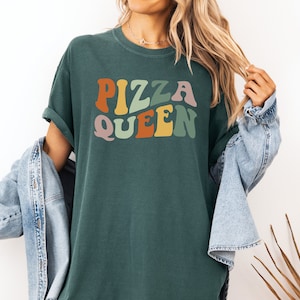 May include: A dark green t-shirt with the text "Pizza Queen" in colorful retro-style lettering.