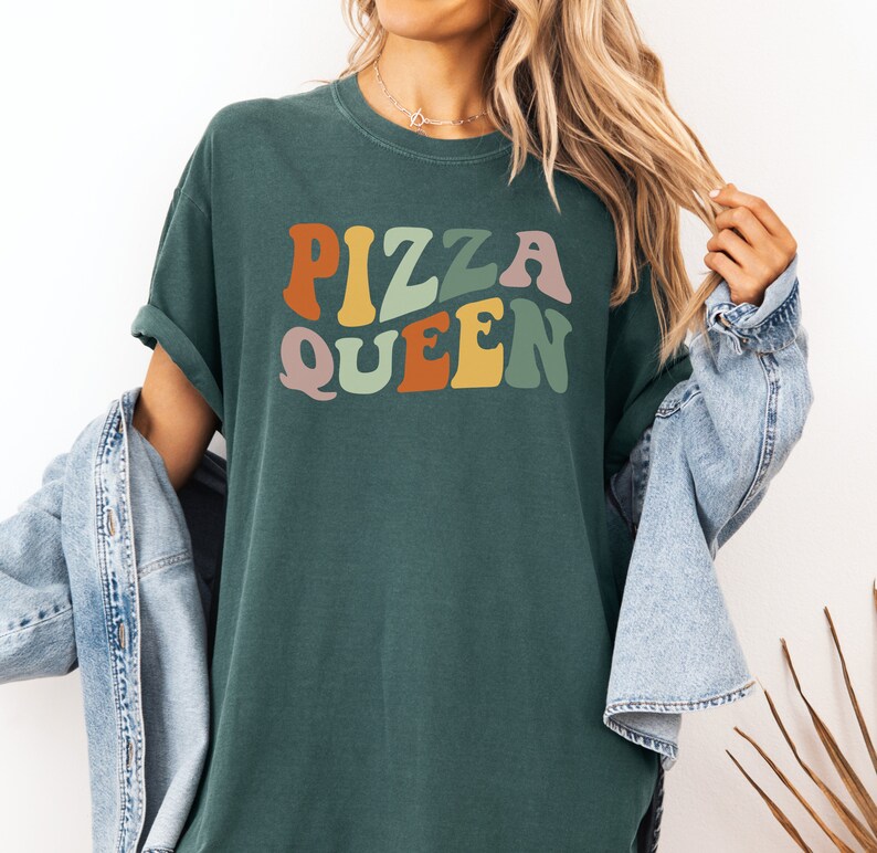 May include: A dark green t-shirt with the text "Pizza Queen" in colorful retro-style lettering.