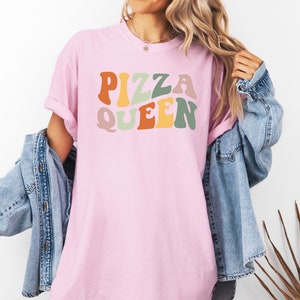 May include: A pink t-shirt with the text "PIZZA QUEEN" in colorful retro-style lettering.
