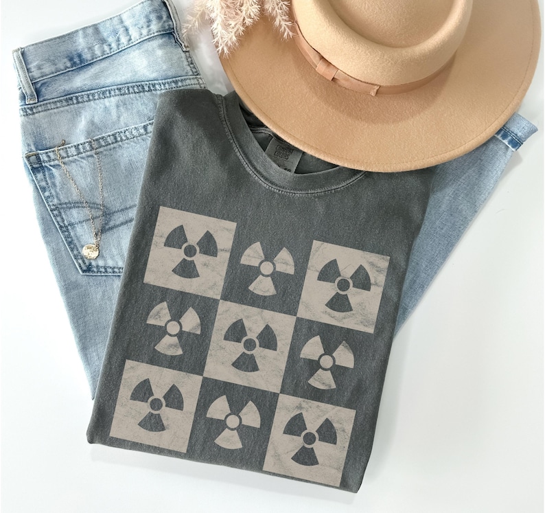 May include: A dark gray t-shirt with a checkered pattern of nine beige radiation symbols.