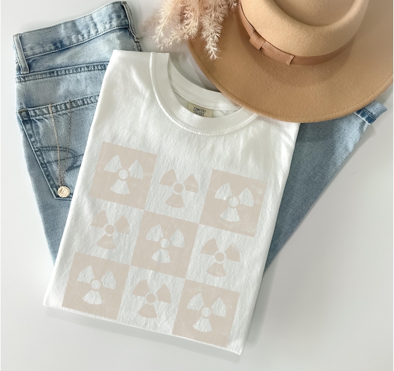 May include: White t-shirt with a beige pattern of repeating radiation symbols.