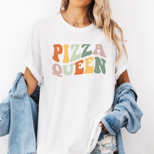 May include: White t-shirt with the text "PIZZA QUEEN" in colorful retro-style lettering.