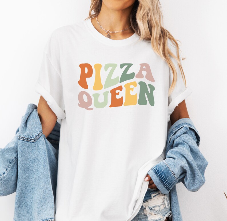 May include: White t-shirt with the text "PIZZA QUEEN" in colorful retro-style lettering.