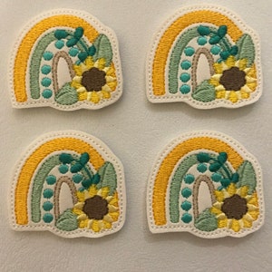 May include: Four embroidered patches featuring a rainbow with a sunflower and green leaves. The rainbow is yellow, green, and blue. The sunflower is yellow with a brown center. The leaves are green.