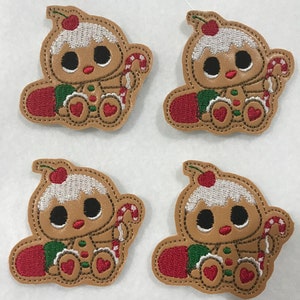 May include: Four identical embroidered patches featuring a tan gingerbread character with large black eyes, a white icing hat topped with a red cherry, and a red and white candy cane. The character wears green and red accents on its body.