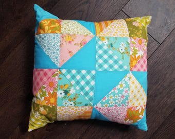 Puede incluir: Cojín cuadrado de patchwork con fondo turquesa y coloridos estampados florales y geométricos. El cojín presenta una variedad de telas en tonos rosa, naranja, verde y azul, creando un diseño vibrante y alegre.