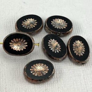 May include: Five oval-shaped glass beads with a black background and a copper-colored flower design.
