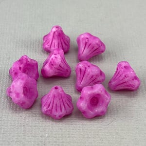 Peut inclure: Dix perles en verre rose avec un motif floral. Les perles sont en forme de cône avec une base large et plate et un sommet pointu. Les perles ont une surface texturée et une finition brillante.